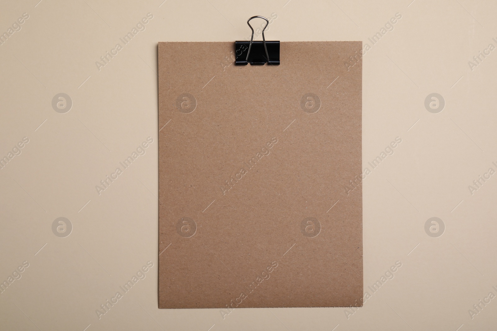 Photo of Sheet of brown paper with clip on beige background, top view