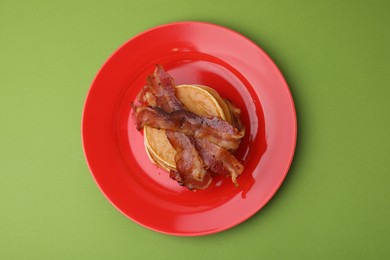Delicious pancakes with bacon on green table, top view