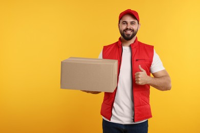 Happy young courier with parcel showing thumb up on orange background, space for text