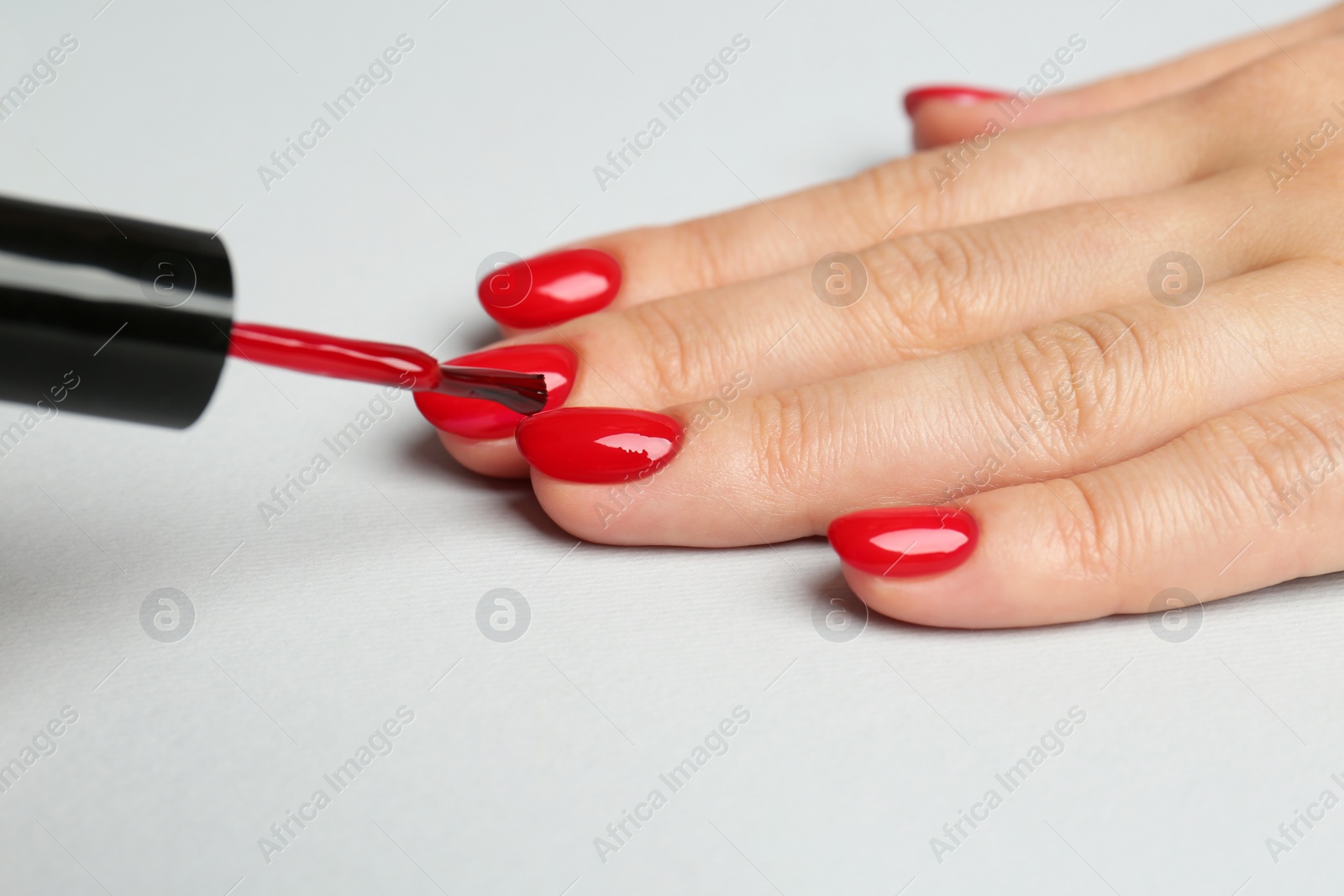 Photo of Woman painting nails with red polish on white background, closeup