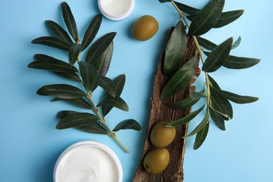 Flat lay composition with jars of cream and olives on light blue background