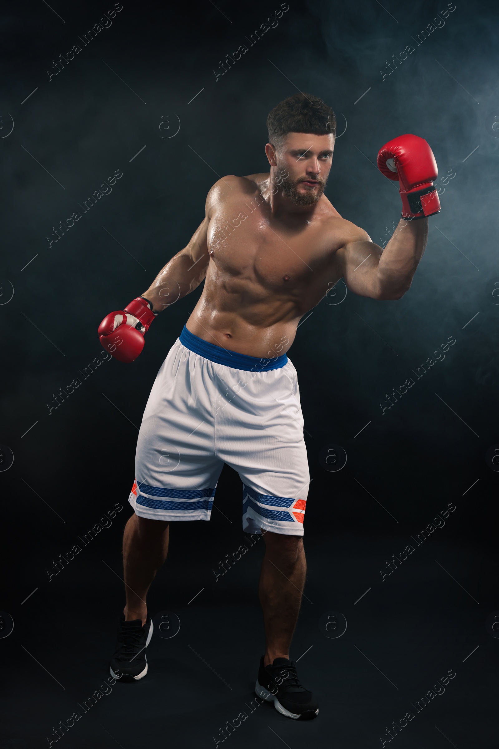 Photo of Man wearing boxing gloves fighting in smoke on black background