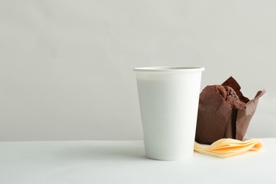 Takeaway paper coffee cup and tasty muffin on white background. Space for design