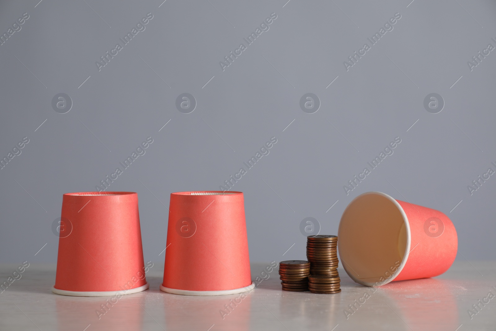 Photo of Shell game. Three red cups and coins on light table