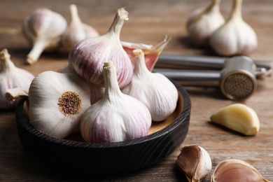 Photo of Fresh organic garlic in bowl on wooden table, closeup