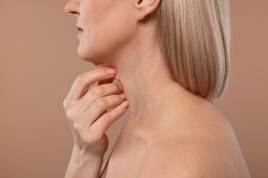 Mature woman touching her neck on beige background, closeup
