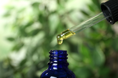 Essential oil dripping from pipette into bottle on blurred background, closeup