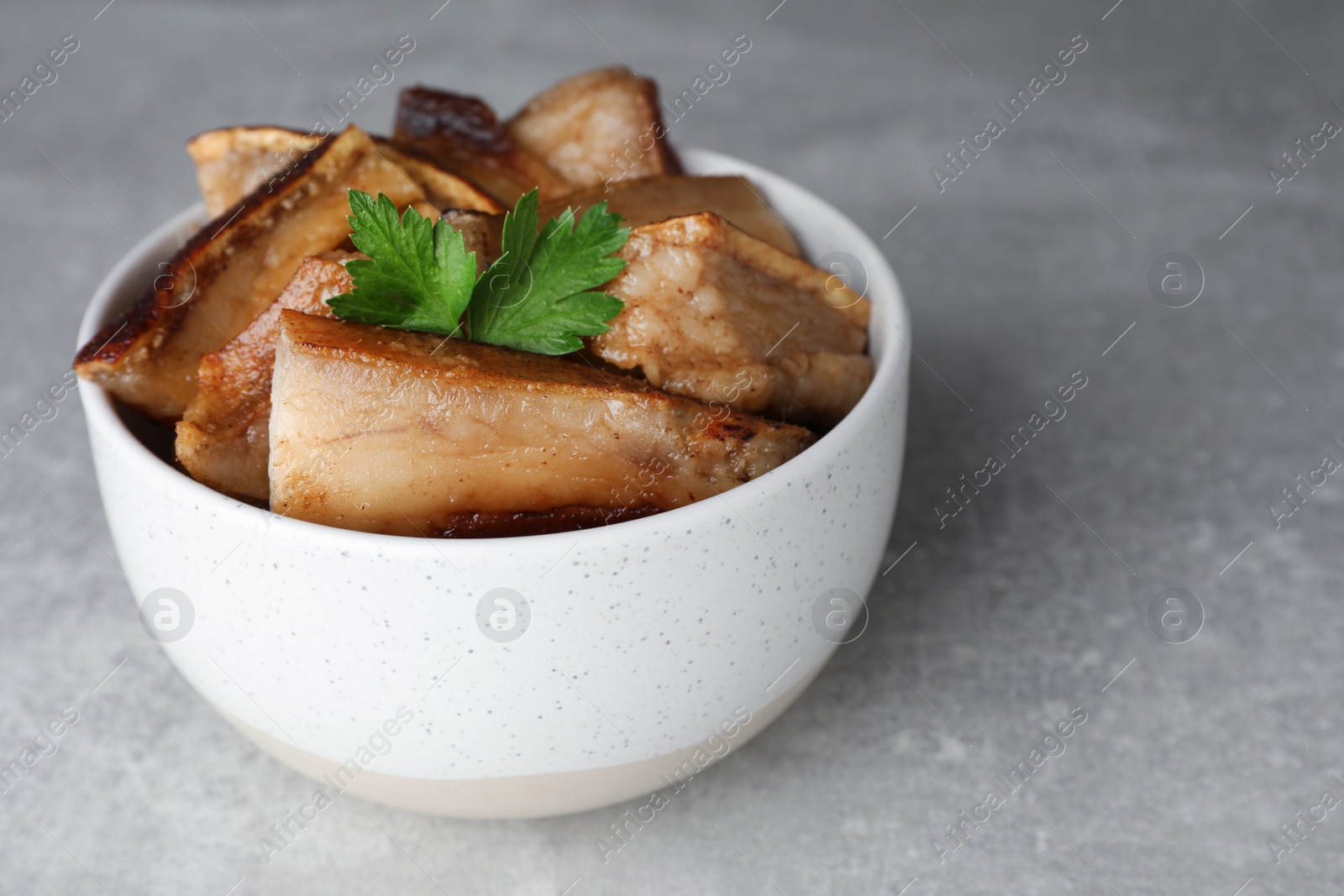 Photo of Bowl with tasty fried pork fatback slices on light grey table, space for text