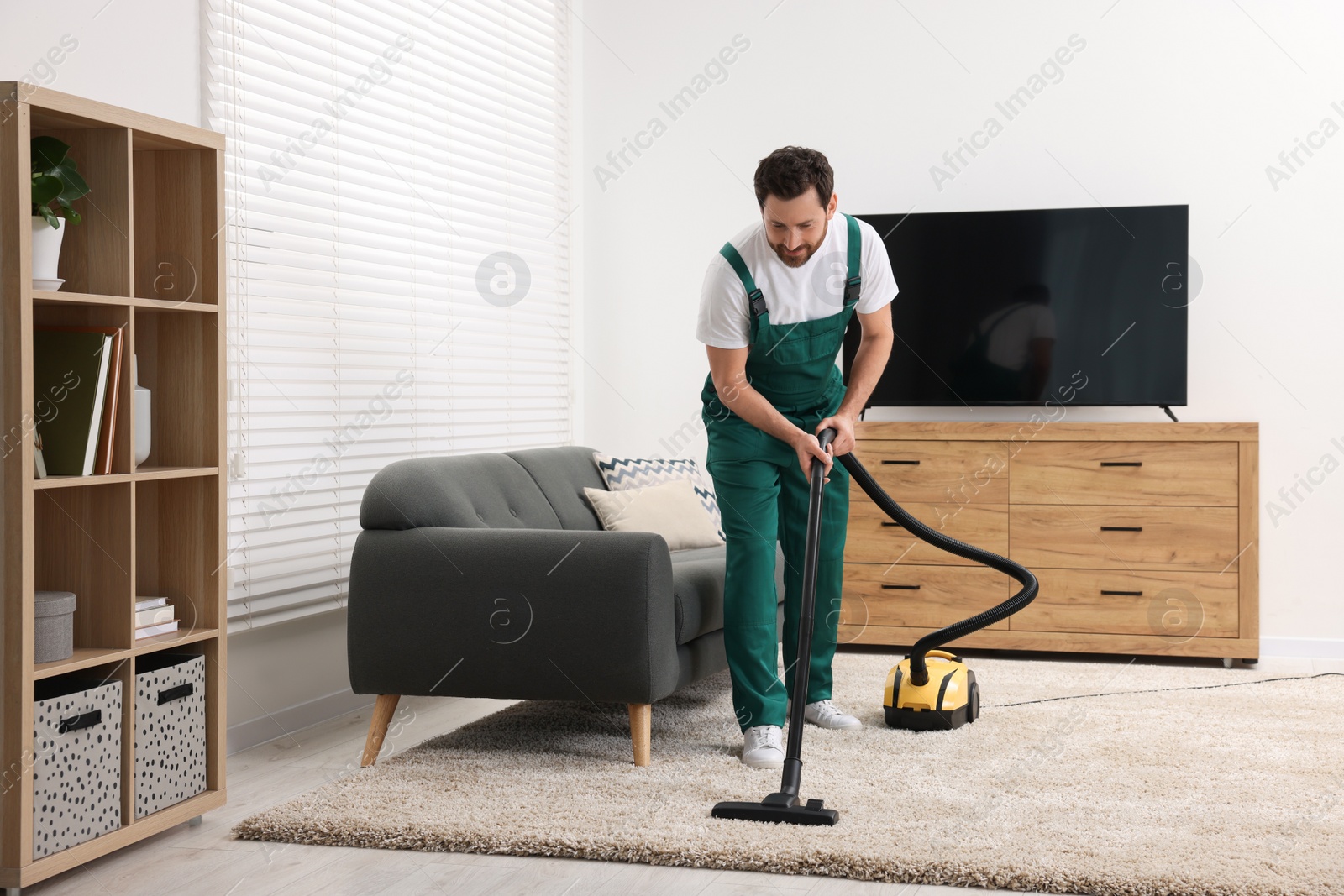 Photo of Dry cleaner's employee hoovering carpet with vacuum cleaner in room