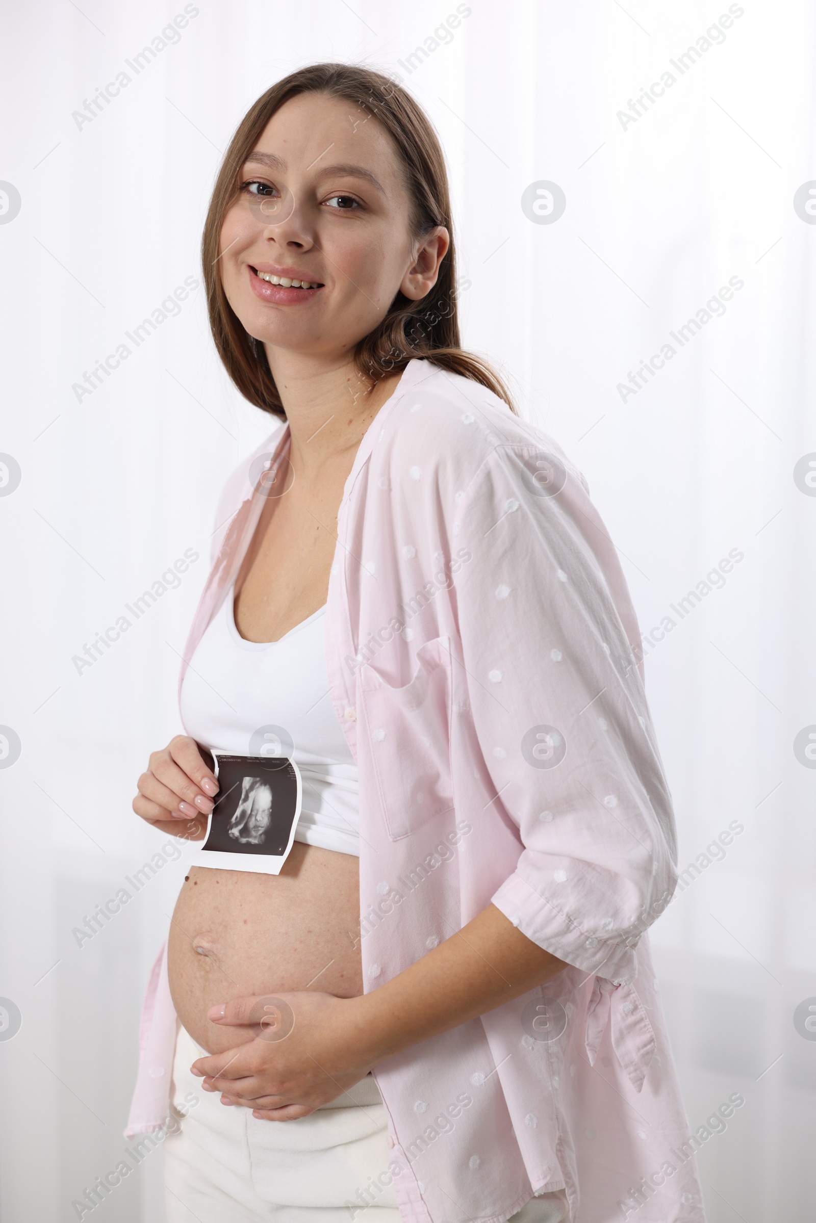 Photo of Beautiful pregnant woman with ultrasound picture of baby near window indoors