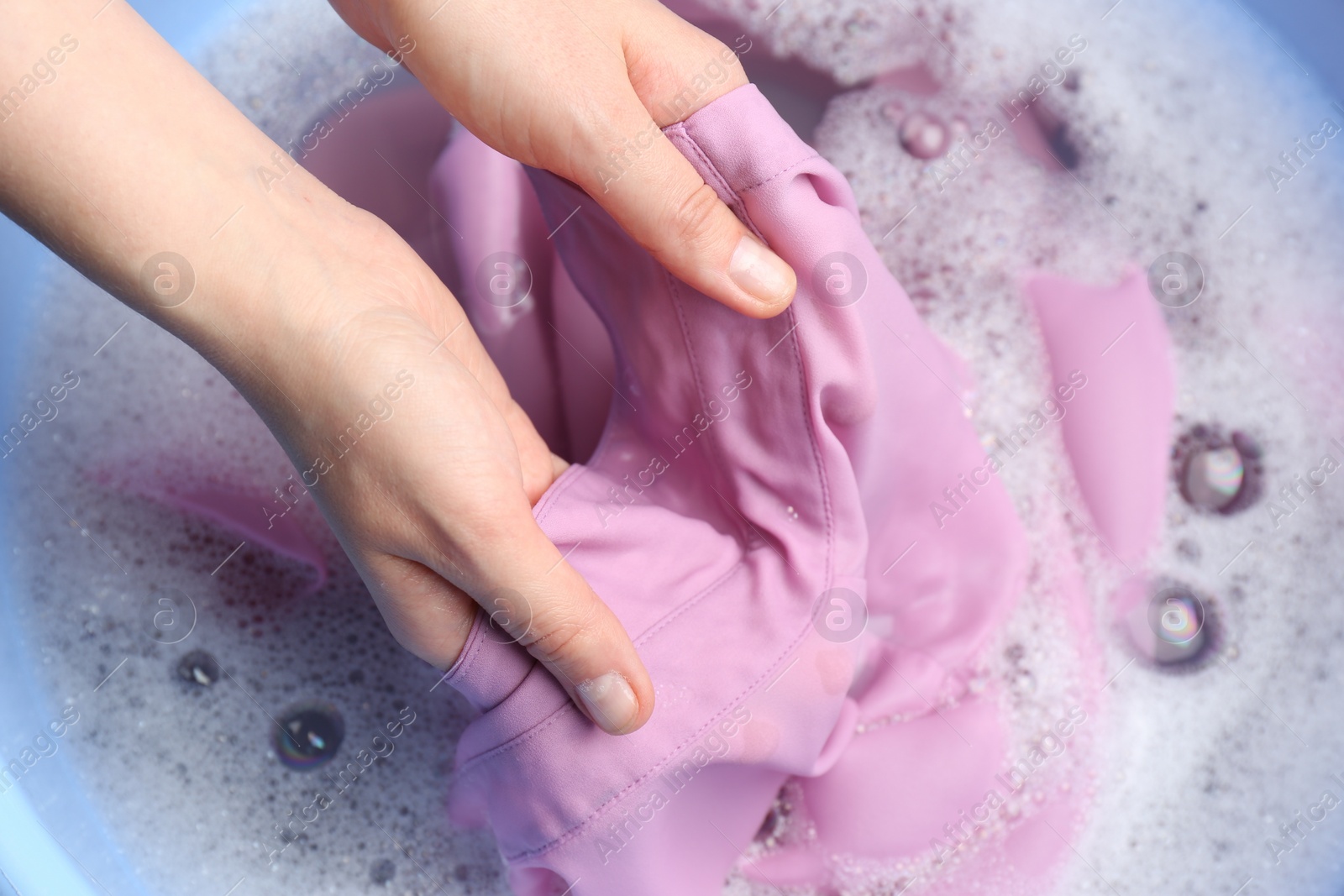 Photo of Top view of woman hand washing color clothing in suds, closeup