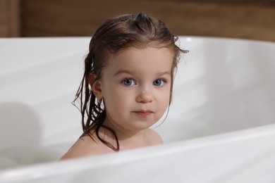 Photo of Cute little girl washing hair with shampoo in bathroom