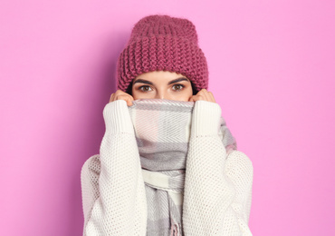 Photo of Young woman wearing warm sweater, scarf and hat on pink background. Winter season