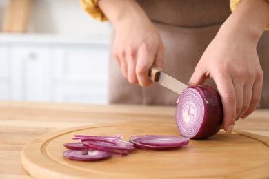 Photo of Woman cutting red onion into rings at wooden table, closeup