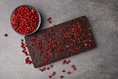 Photo of Delicious chocolate bar and red peppercorns on grey textured table, flat lay