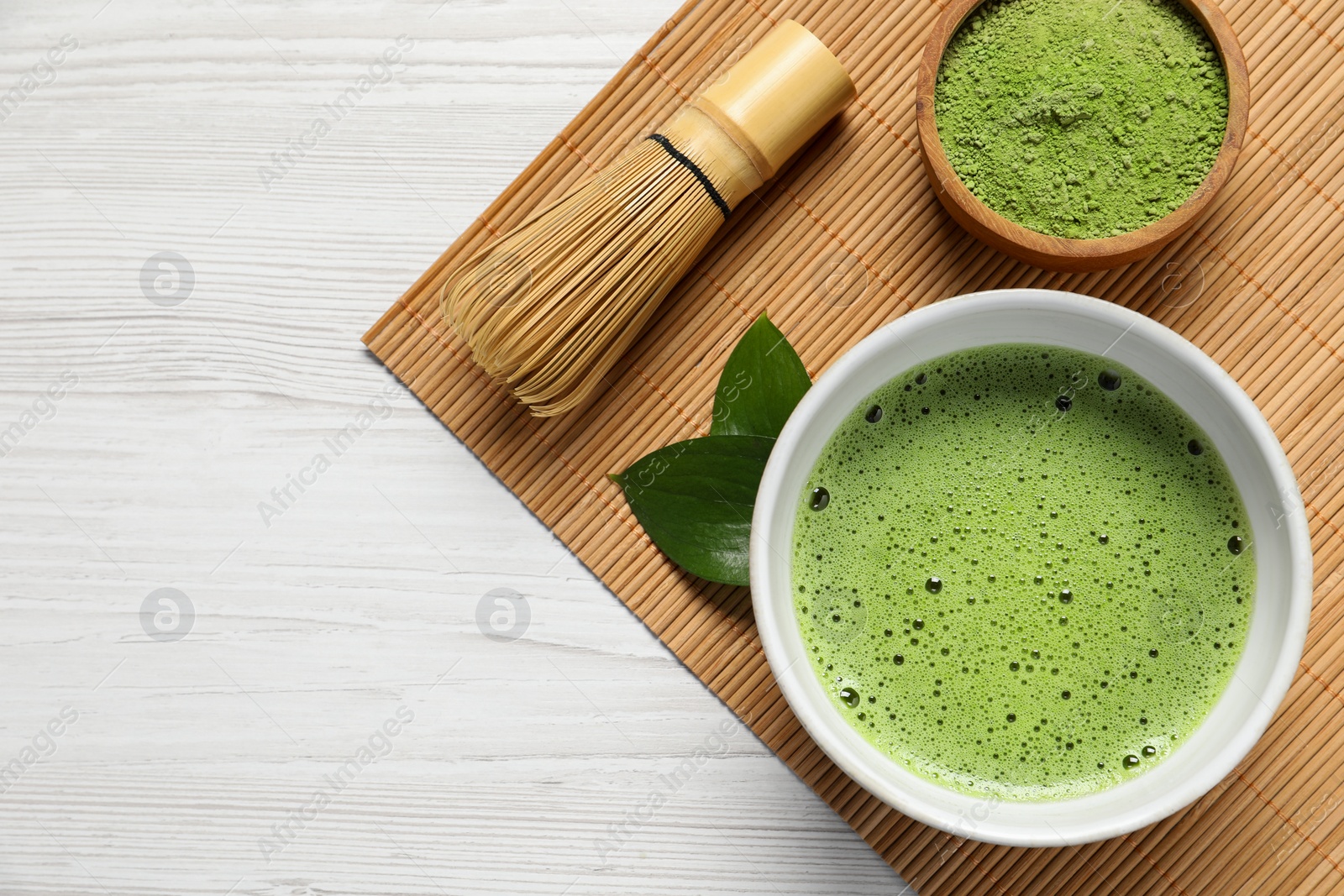 Photo of Cup of fresh matcha tea, bamboo whisk and green powder on white wooden table, top view. Space for text