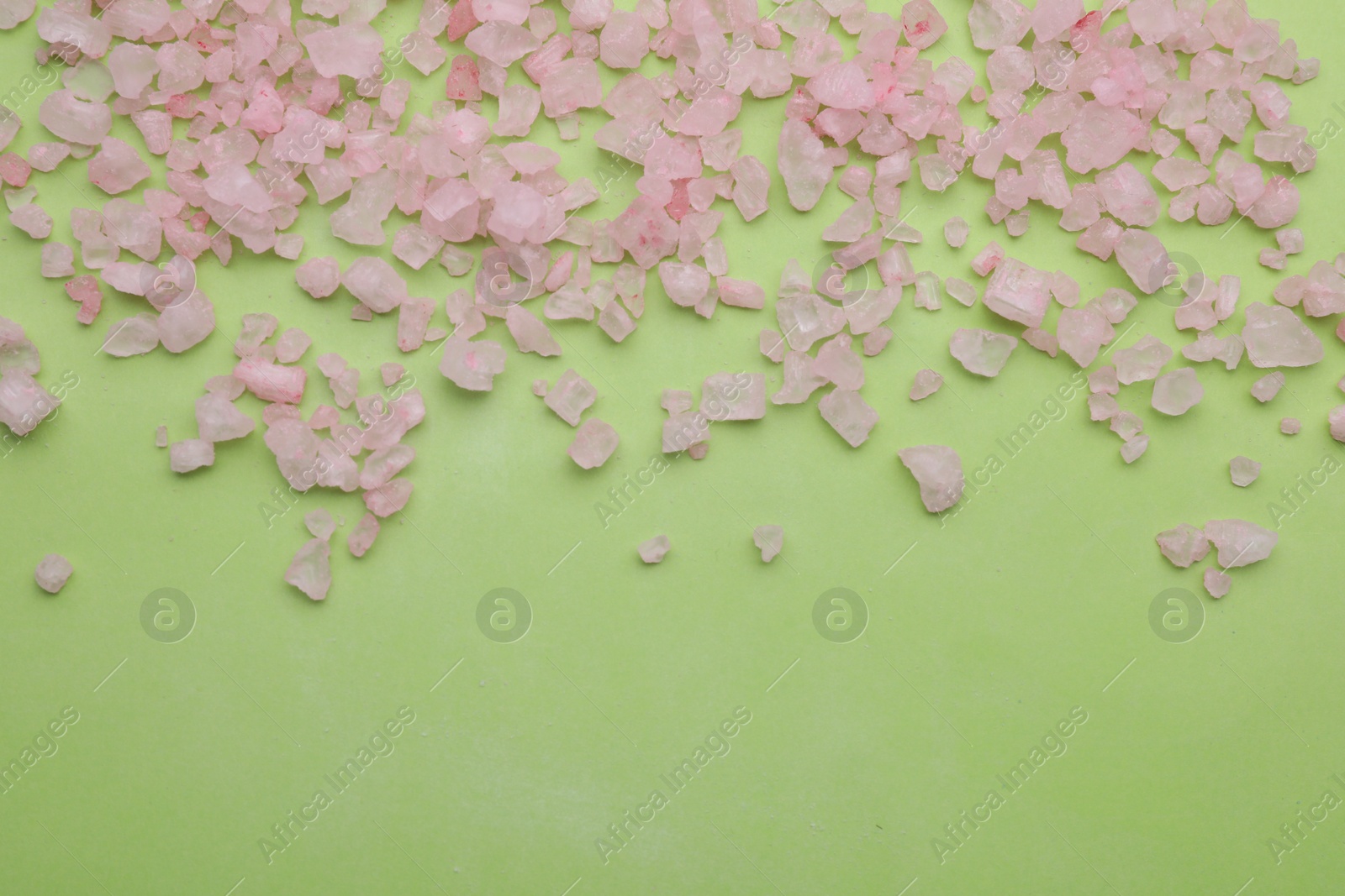 Photo of Pink sea salt on light green background, top view. Space for text