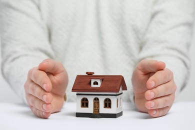 Photo of Home security concept. Man with house model at white table, closeup