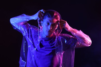 Photo of Young man wearing clear coat on dark background in neon lights