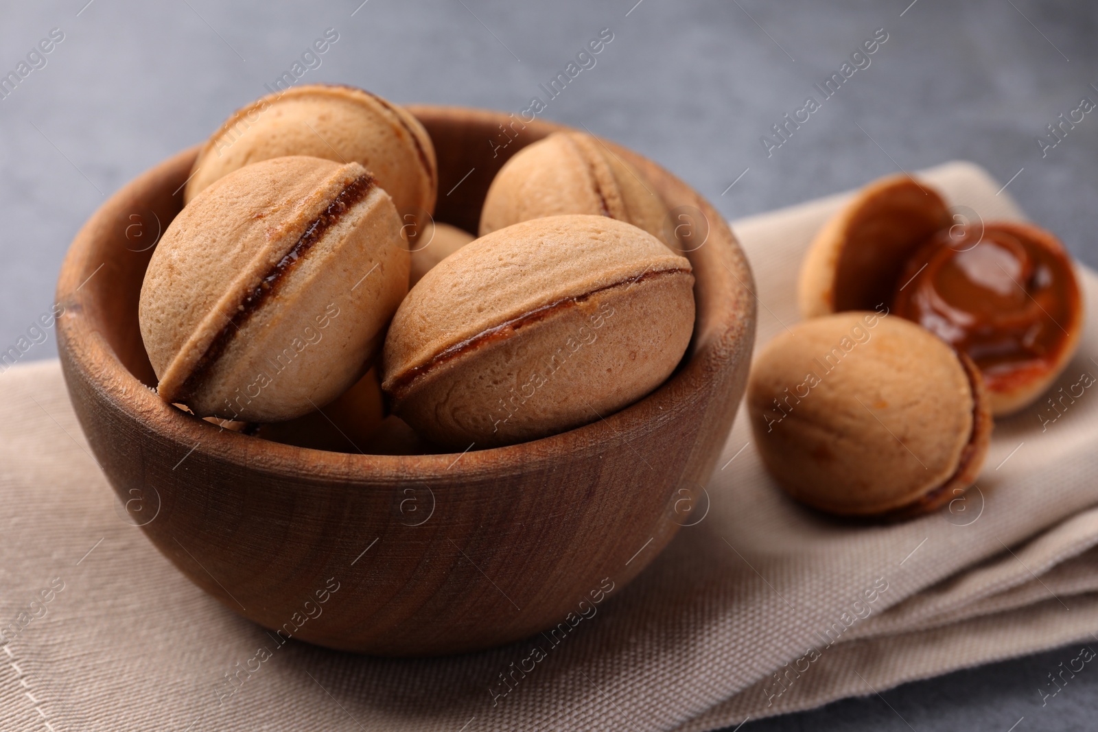 Photo of Delicious nut shaped cookies with boiled condensed milk in wooden bowl on table, closeup