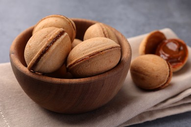 Photo of Delicious nut shaped cookies with boiled condensed milk in wooden bowl on table, closeup