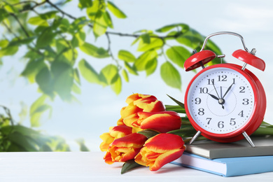 Image of Red alarm clock, books and tulips on table against blurred background, space for text. Spring time