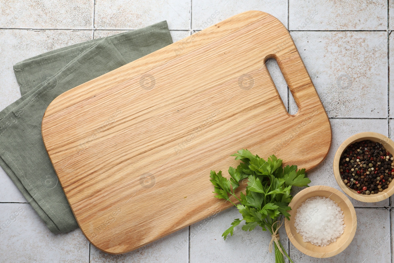 Photo of Cutting board, salt, pepper and parsley on white tiled table, flat lay. Space for text