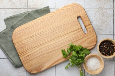 Photo of Cutting board, salt, pepper and parsley on white tiled table, flat lay. Space for text