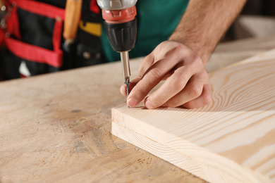 Photo of Professional carpenter twisting screw with drill at workbench, closeup