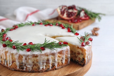 Traditional Christmas cake decorated with rosemary and pomegranate seeds on white table, closeup