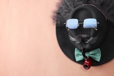 Photo of Man's face made of artificial mustache, sunglasses and hat on brown background, top view. Space for text