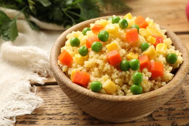 Photo of Tasty millet porridge with vegetables in bowl on wooden table, closeup