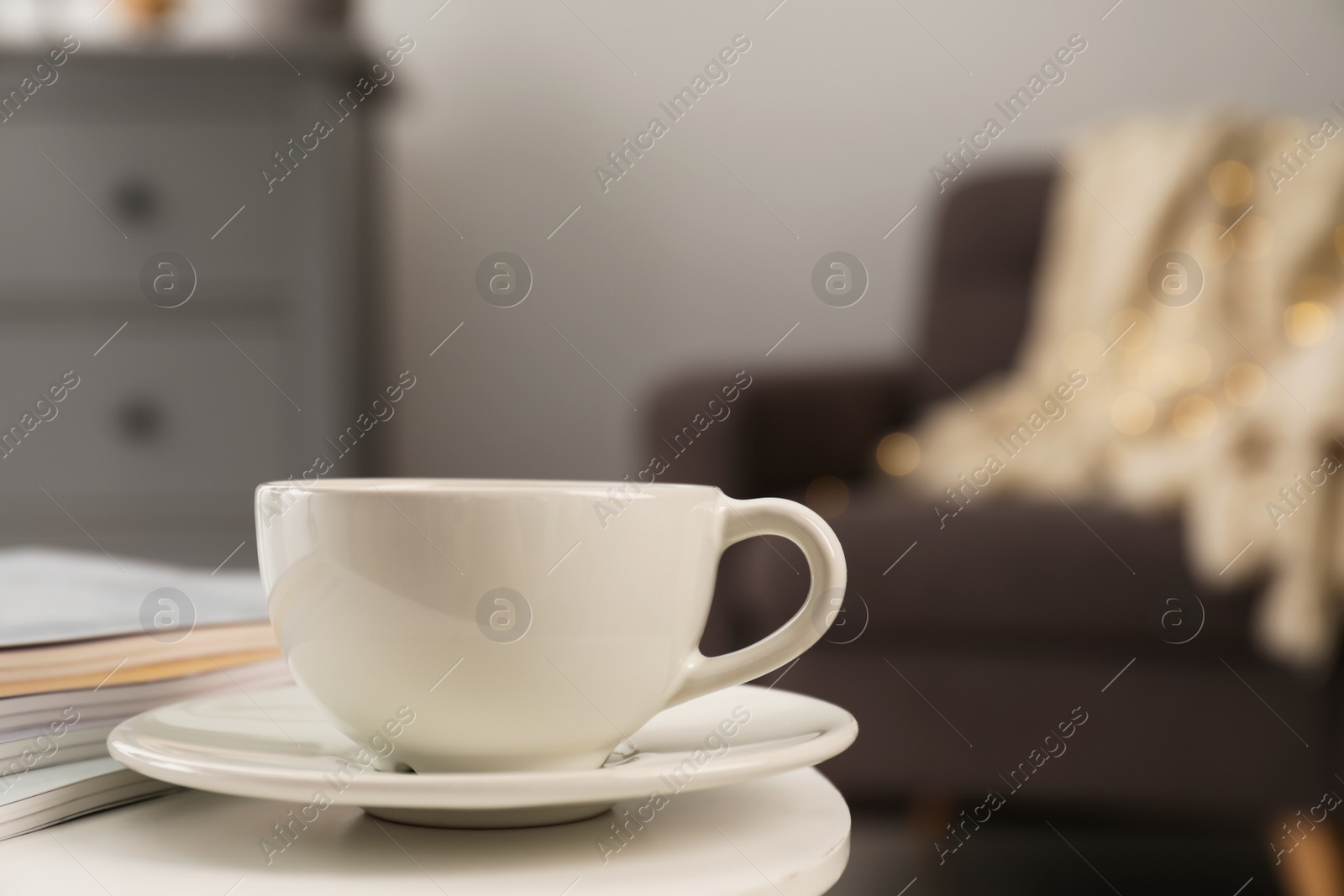 Photo of Cup with drink and stack of magazines on white table in living room, space for text