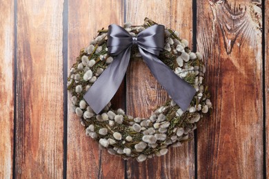 Photo of Wreath made of beautiful willow branches and grey bow on wooden background, top view