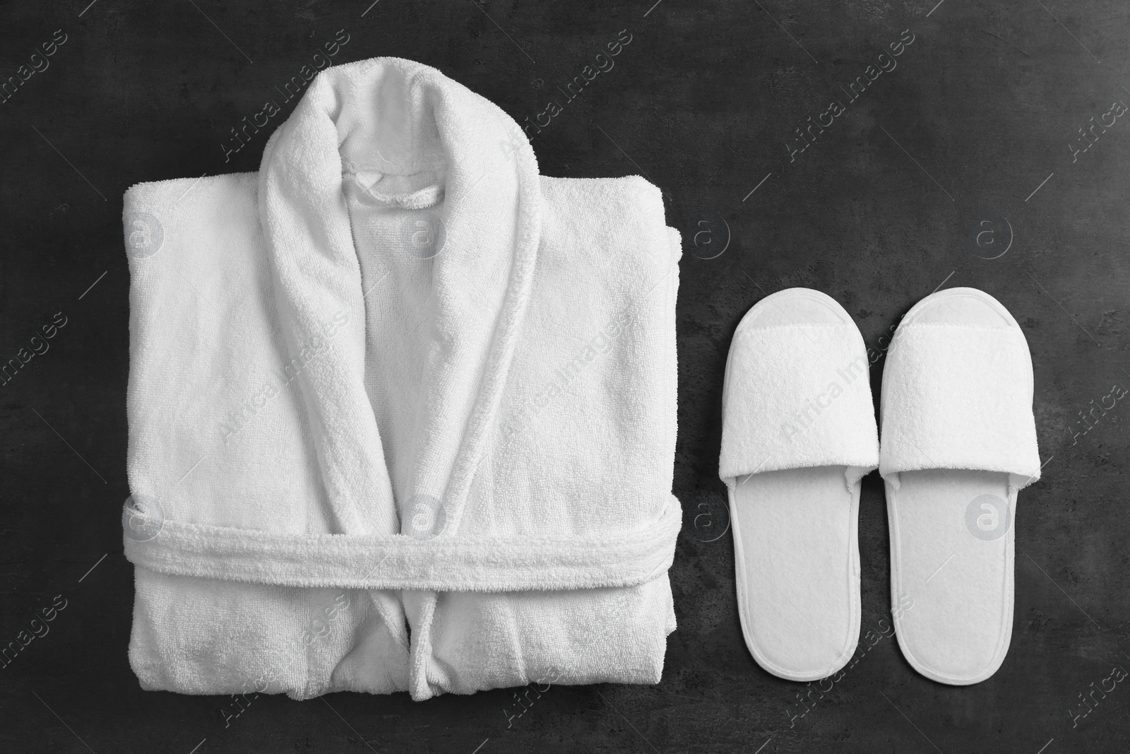 Photo of Clean folded bathrobe and slippers on black stone background, flat lay