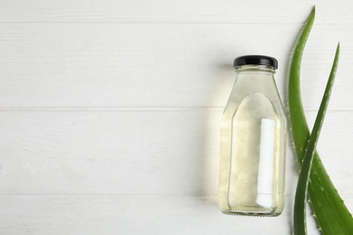 Photo of Fresh aloe drink in bottle and leaves on white wooden table, flat lay. Space for text