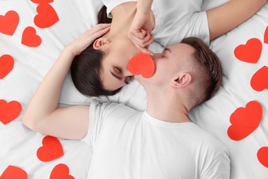 Lovely couple kissing behind decorative heart on bed, top view. Valentine's day celebration