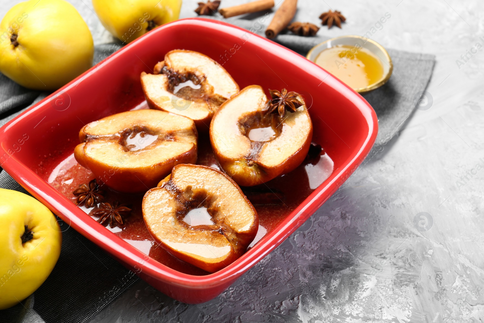 Photo of Tasty baked quinces with honey in dish on grey textured table, closeup