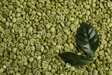 Lush leaves on pile of green coffee beans, flat lay. Space for text