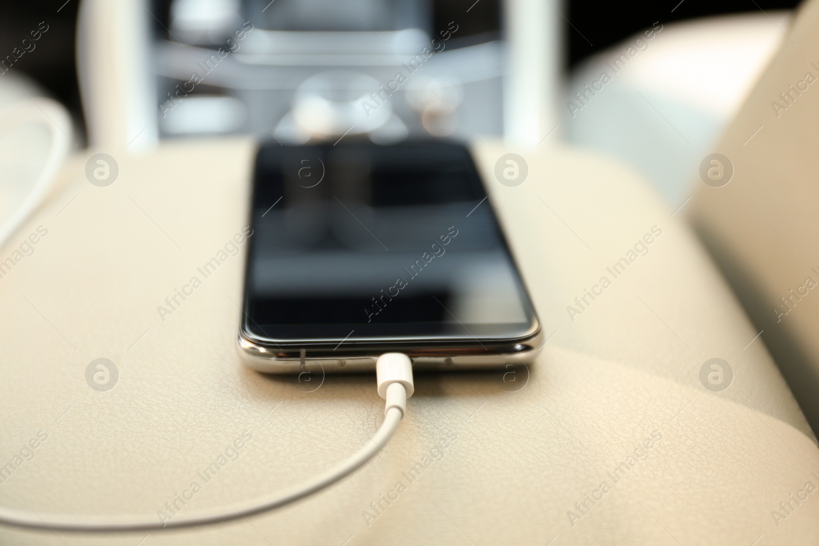 Photo of Mobile phone with charging cable in car, closeup