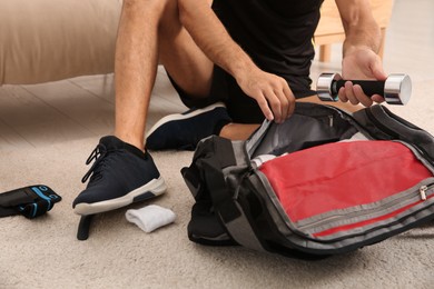 Man packing sports stuff for training into bag indoors, closeup