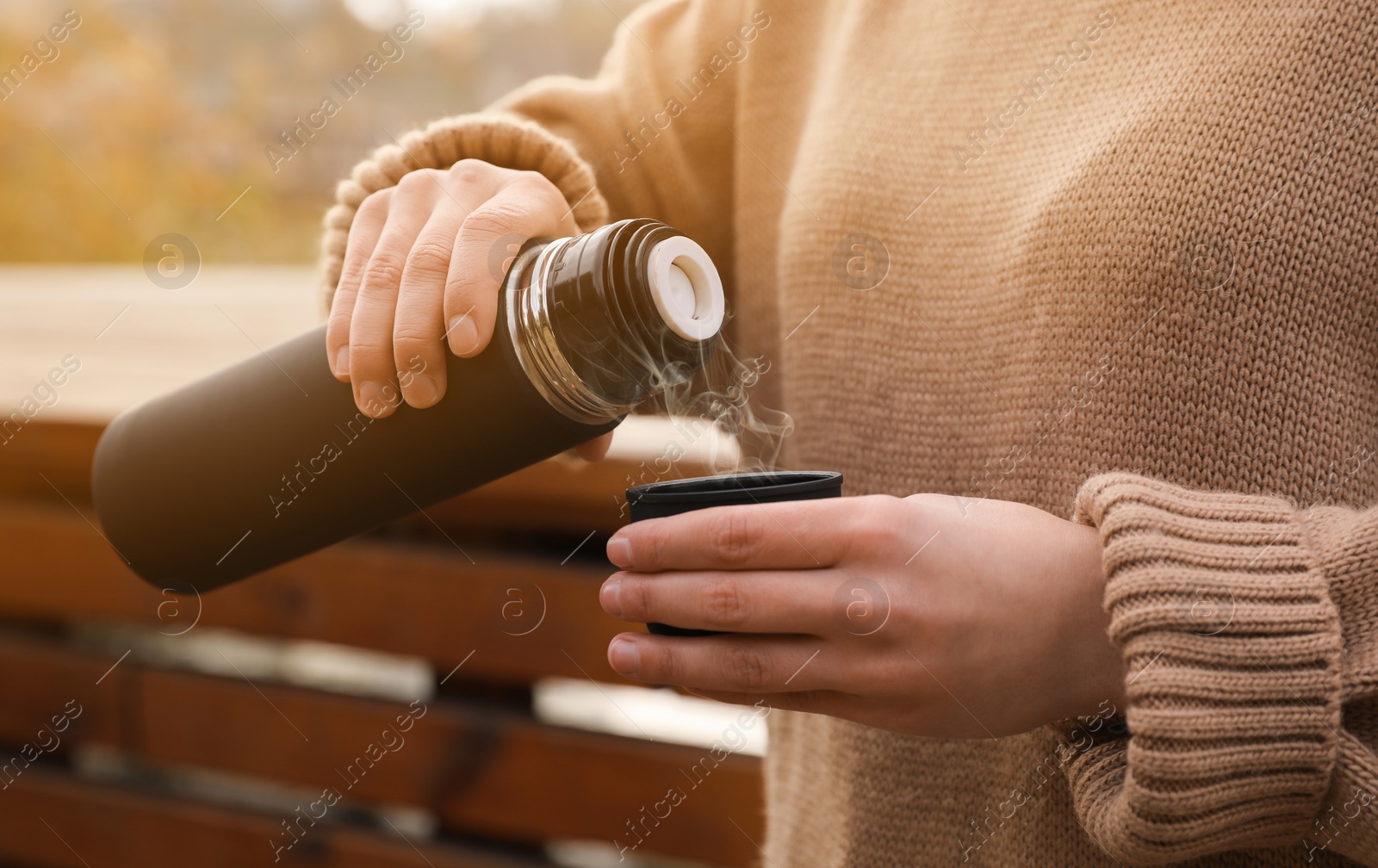 Photo of Woman pouring drink from thermos into cap outdoors, closeup