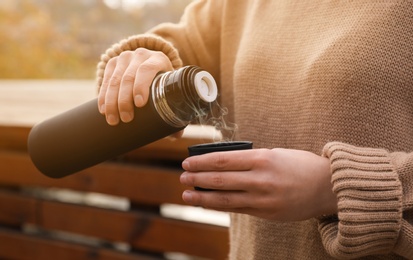 Photo of Woman pouring drink from thermos into cap outdoors, closeup