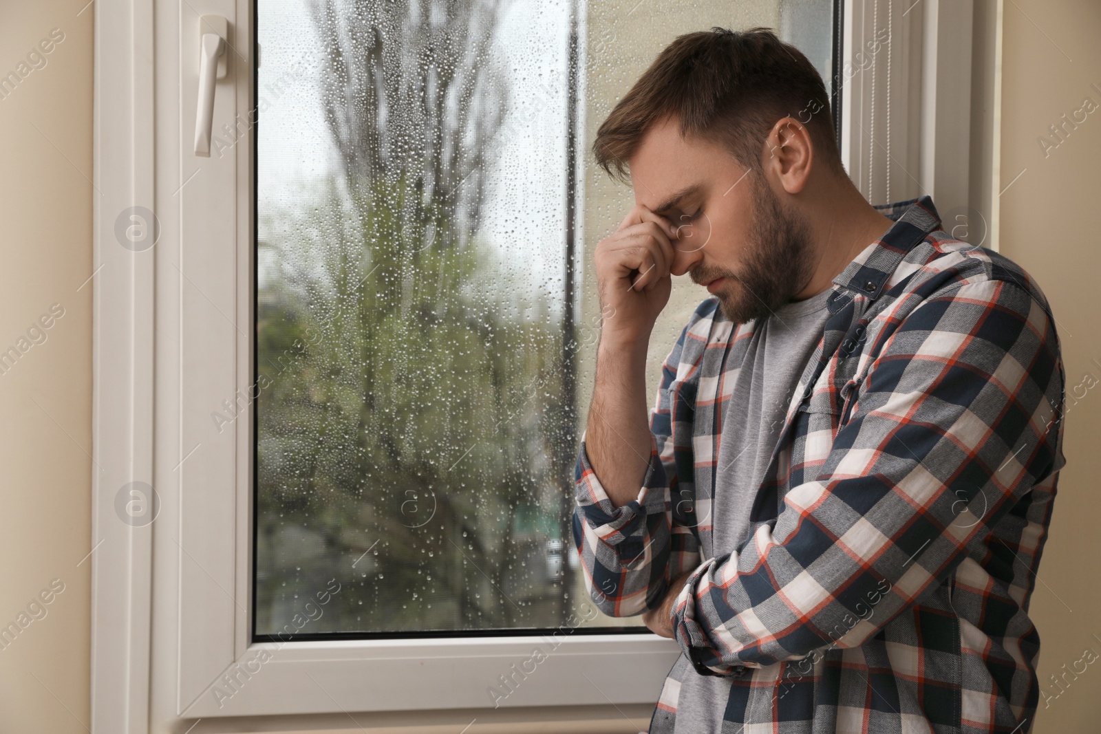 Photo of Depressed man near window at home. Space for text