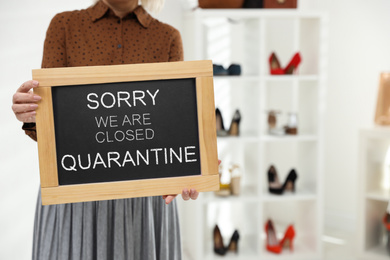 Image of Business owner holding sign with text SORRY WE ARE CLOSED QUARANTINE in boutique, closeup