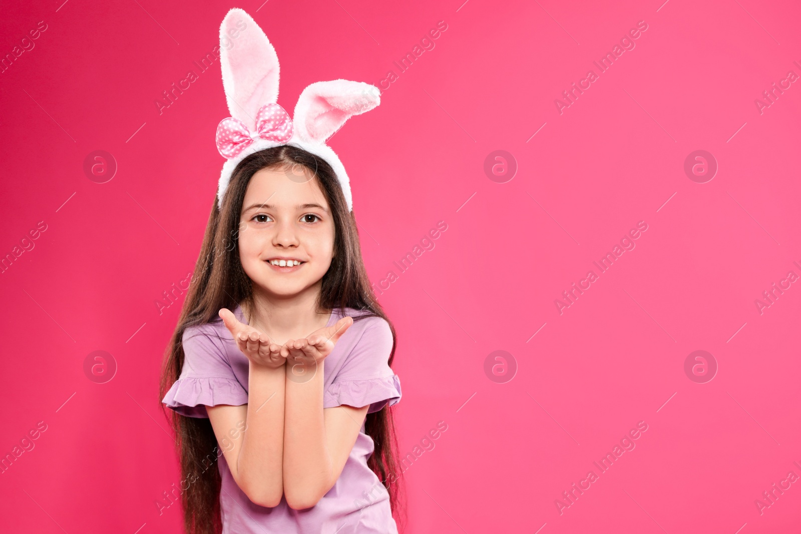 Photo of Portrait of little girl in Easter bunny ears headband on color background, space for text
