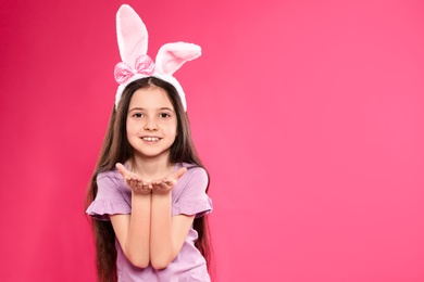 Portrait of little girl in Easter bunny ears headband on color background, space for text