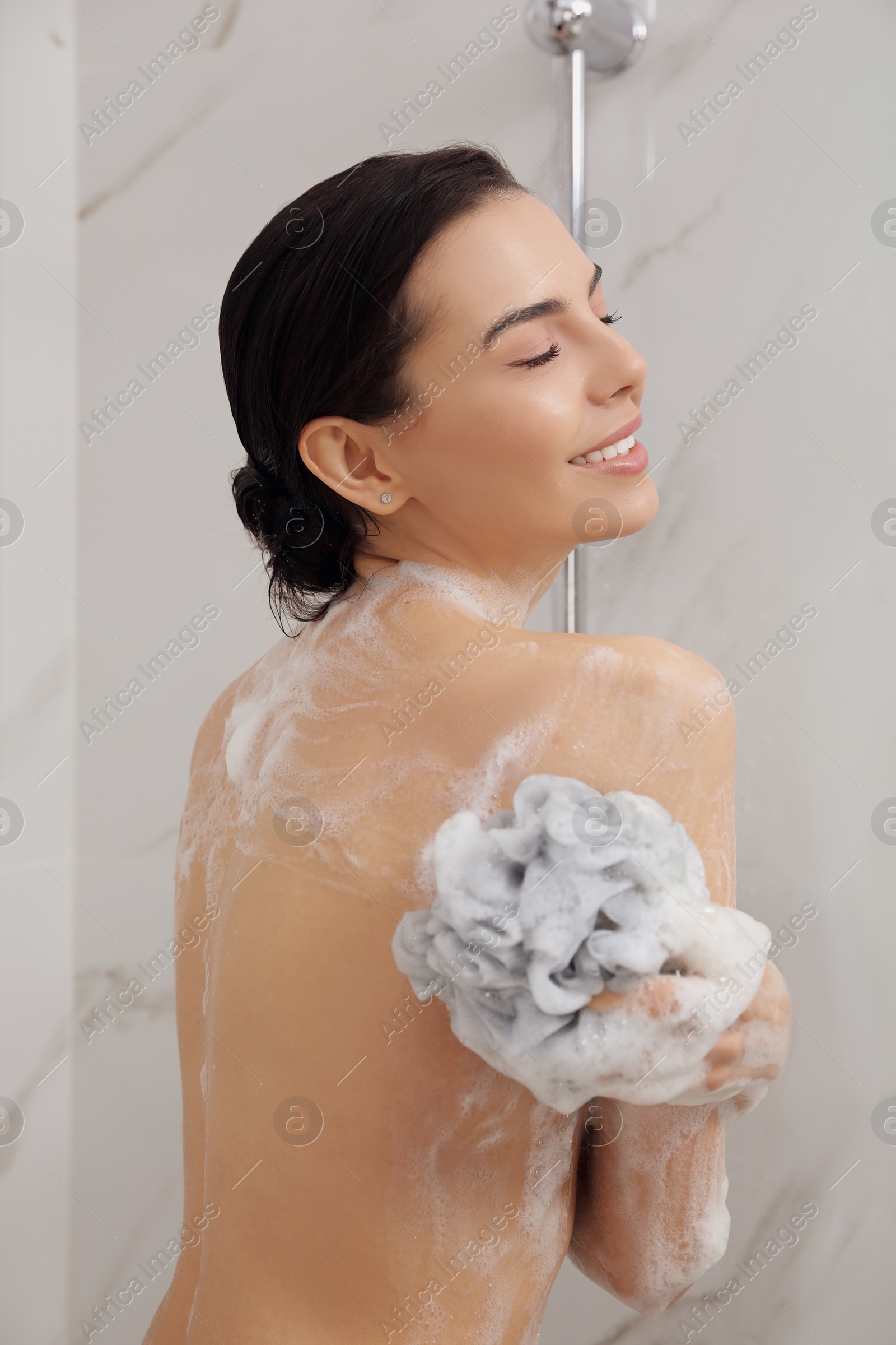 Photo of Young woman with mesh pouf taking shower at home