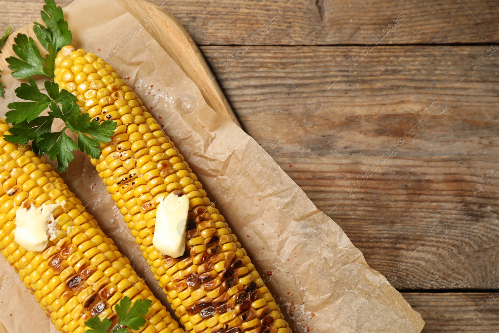 Photo of Tasty grilled corn on wooden table, top view