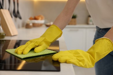 Woman with spray bottle and microfiber cloth cleaning electric stove in kitchen, closeup